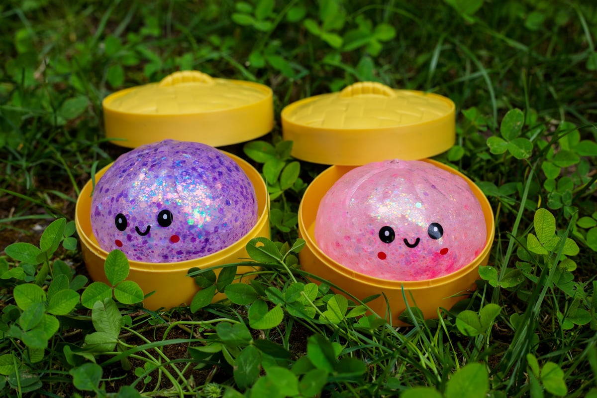 Two kawaii glitter squishy dumpling toys in purple and pink steamer containers