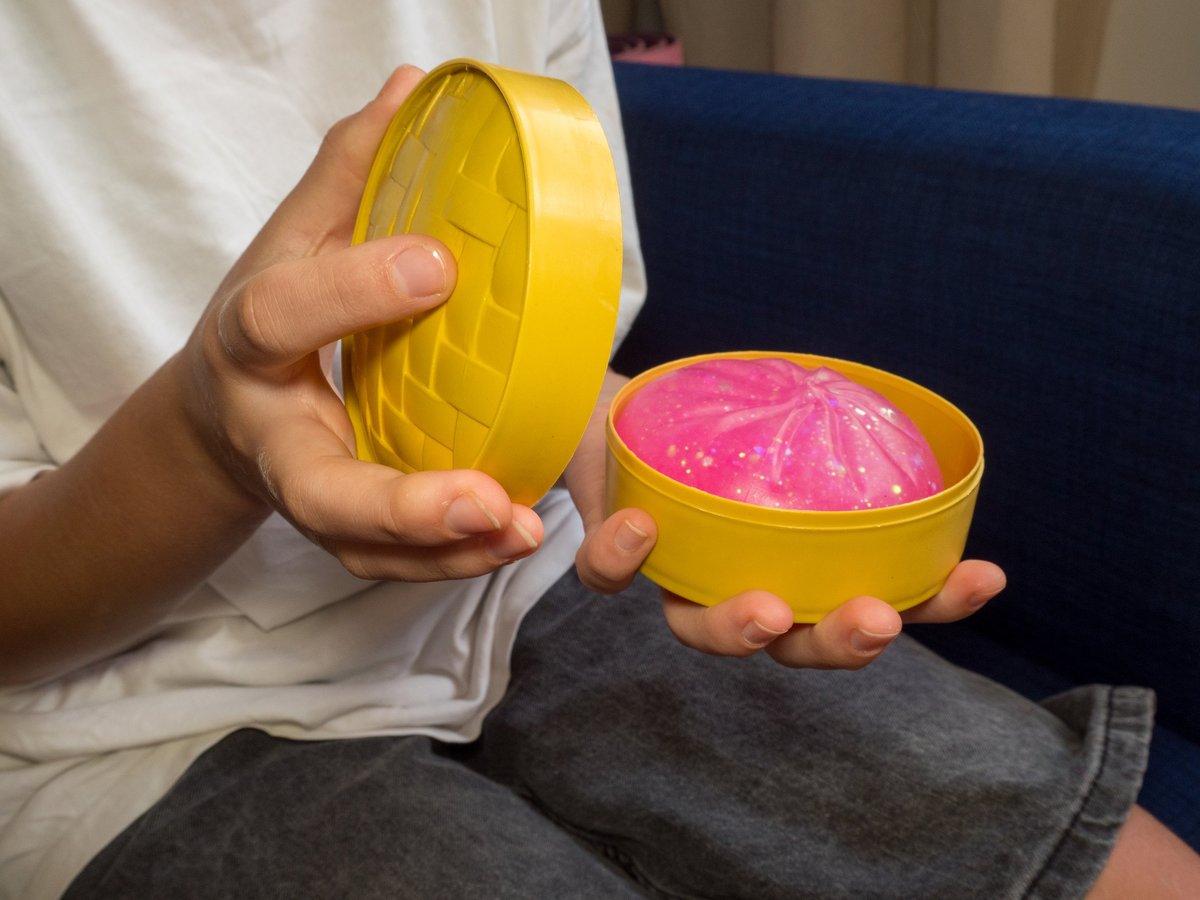Close-up of a child's hands unboxing a pink glittery squishy dumpling toy from a yellow basket