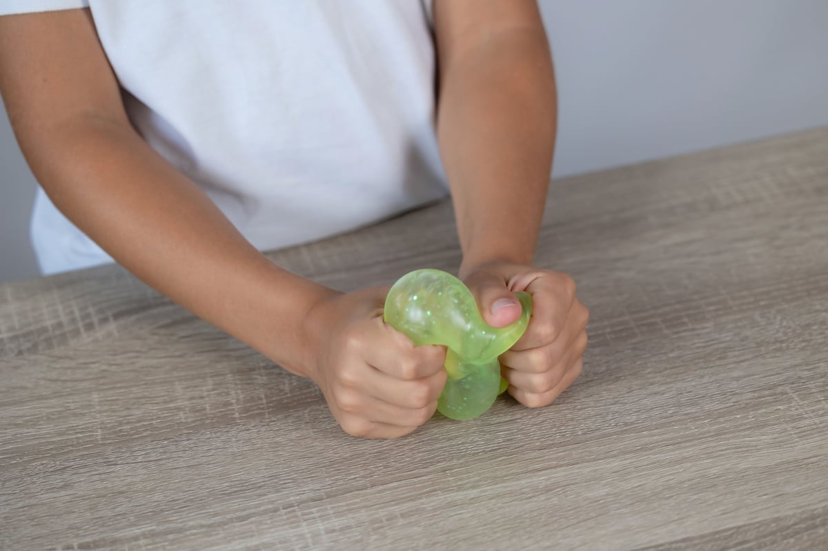 Child's hands squeezing a translucent green sensory stress toy on a woodgrain table